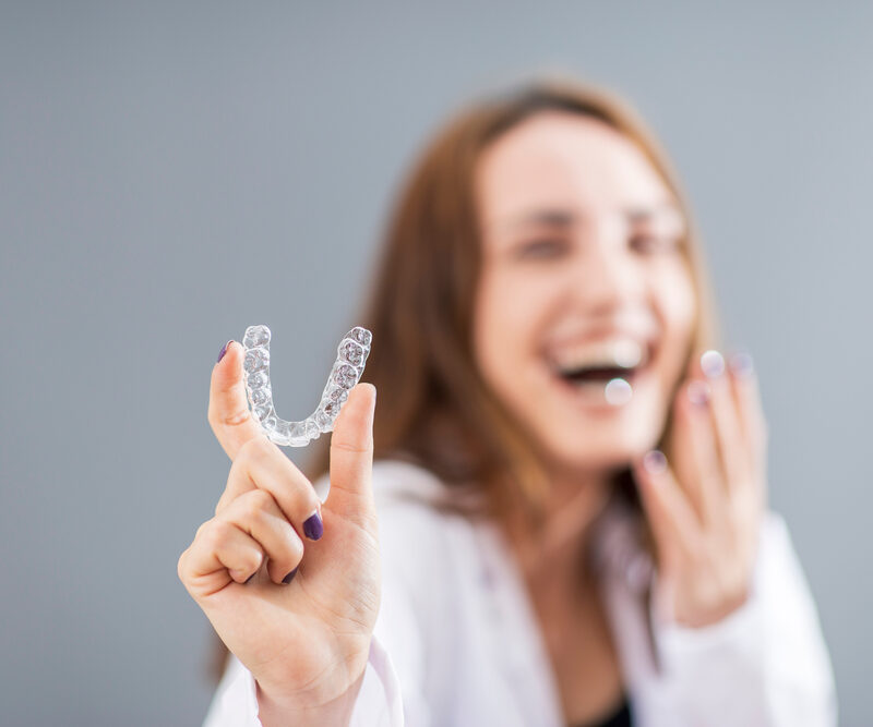 Laughing woman holding up a clear aligner, illustrating Invisalign questions to ask a cosmetic dentist in La Mesa, CA