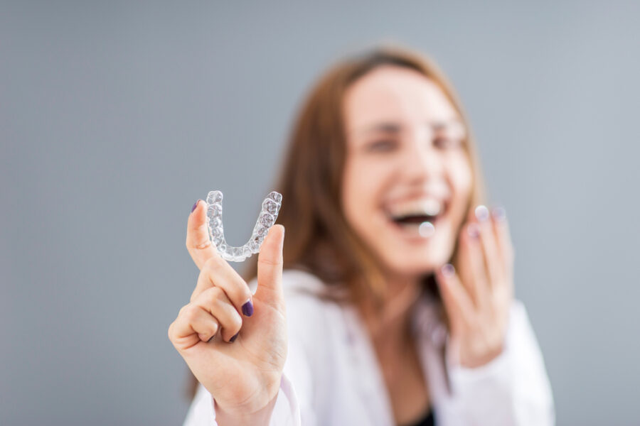 Laughing woman holding up a clear aligner, illustrating Invisalign questions to ask a cosmetic dentist in La Mesa, CA
