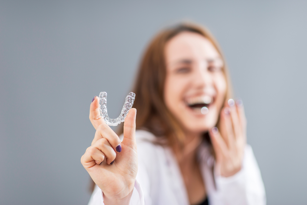 Laughing woman holding up a clear aligner, illustrating Invisalign questions to ask a cosmetic dentist in La Mesa, CA