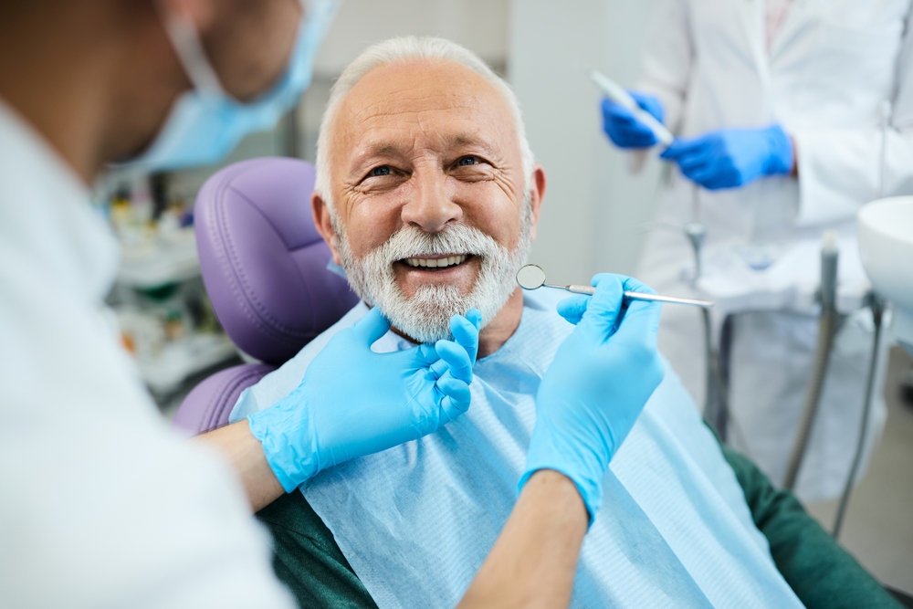 Senior Patient Dental Exam, Denture Care in La Mesa, CA Smiling senior man with a white beard in a dental chair during an exam, the first step in exploring dentures in La Mesa, CA