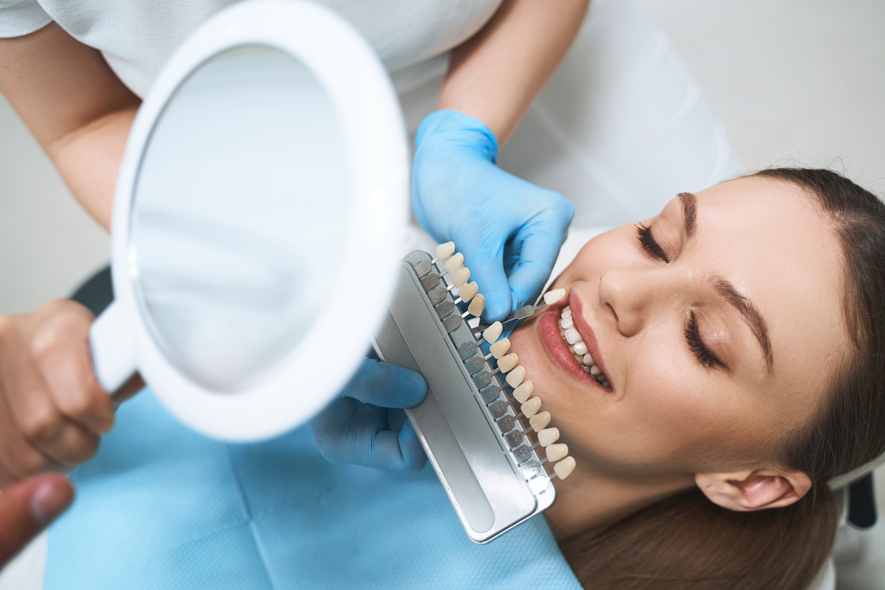 Porcelain Veneers in La Mesa, CA: Shade Matching Dentist holding a veneer shade guide beside a smiling woman's teeth to match color for porcelain veneers in La Mesa, CA