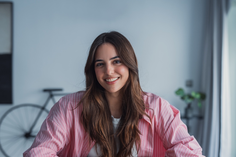 Confident Smile at Home, Dental Implants in La Mesa, CA Smiling woman with long brown hair in a pink striped shirt at home, reflecting the confidence of dental implants in La Mesa, CA