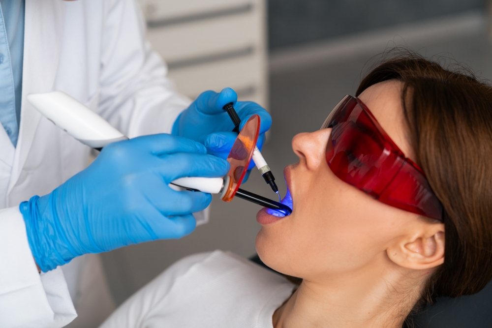 Patient in protective glasses as a dental light glows blue on her teeth, illustrating in-office teeth whitening in La Mesa, CA