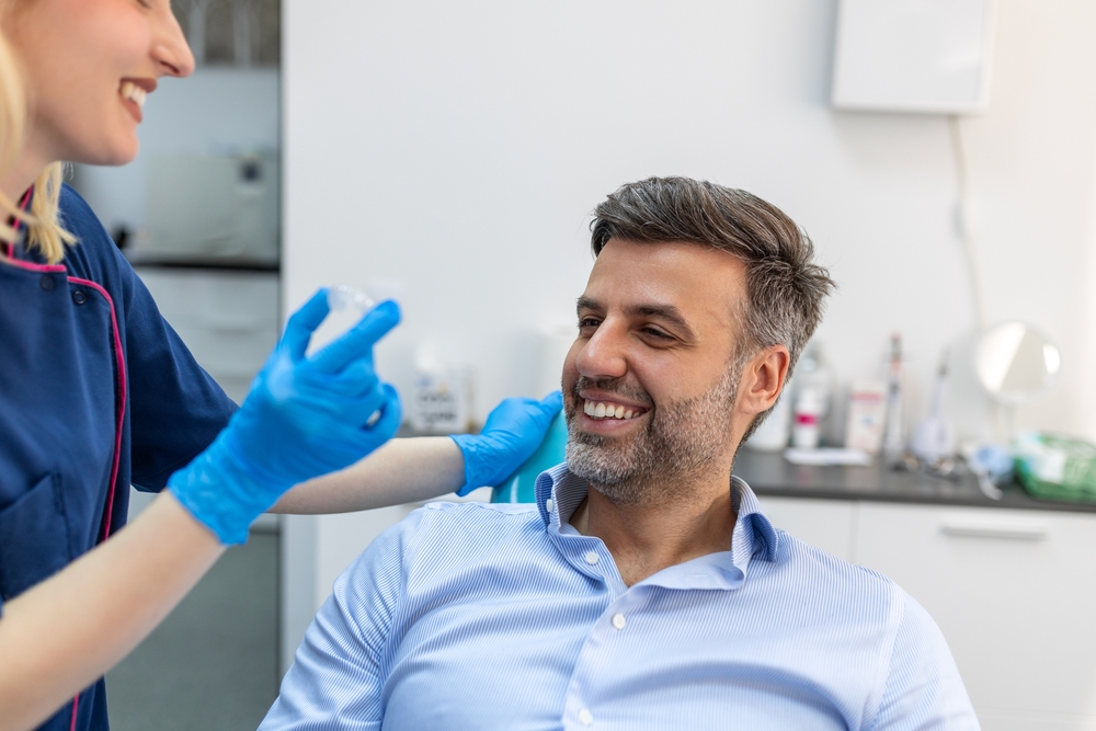 Clear Aligner Consultation, Teeth Straightening in La Mesa, CA Dental team member holding a clear aligner as a smiling man in a dental chair learns about Invisalign in La Mesa, CA