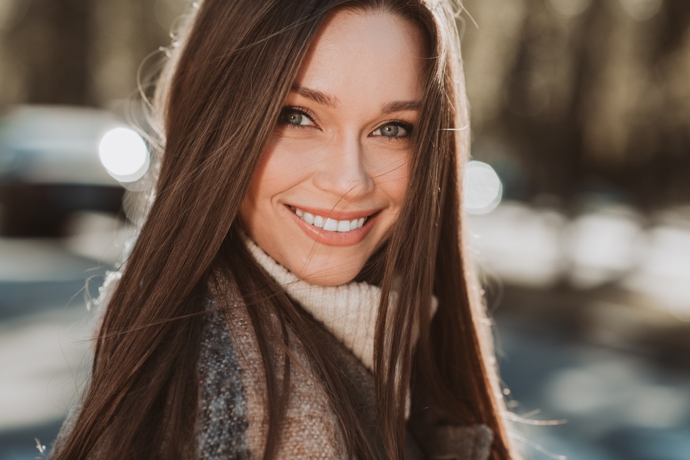 Natural-Looking Results, Tooth Bonding in La Mesa, CA Smiling woman with long brown hair in a turtleneck outdoors, reflecting the natural look of cosmetic bonding in La Mesa, CA