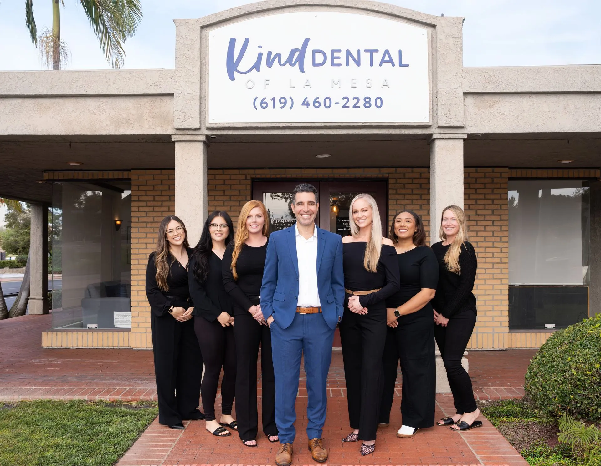 Dr. Maysam and the Kind Dental of La Mesa team smiling on the brick walkway outside their dental office in La Mesa, CA