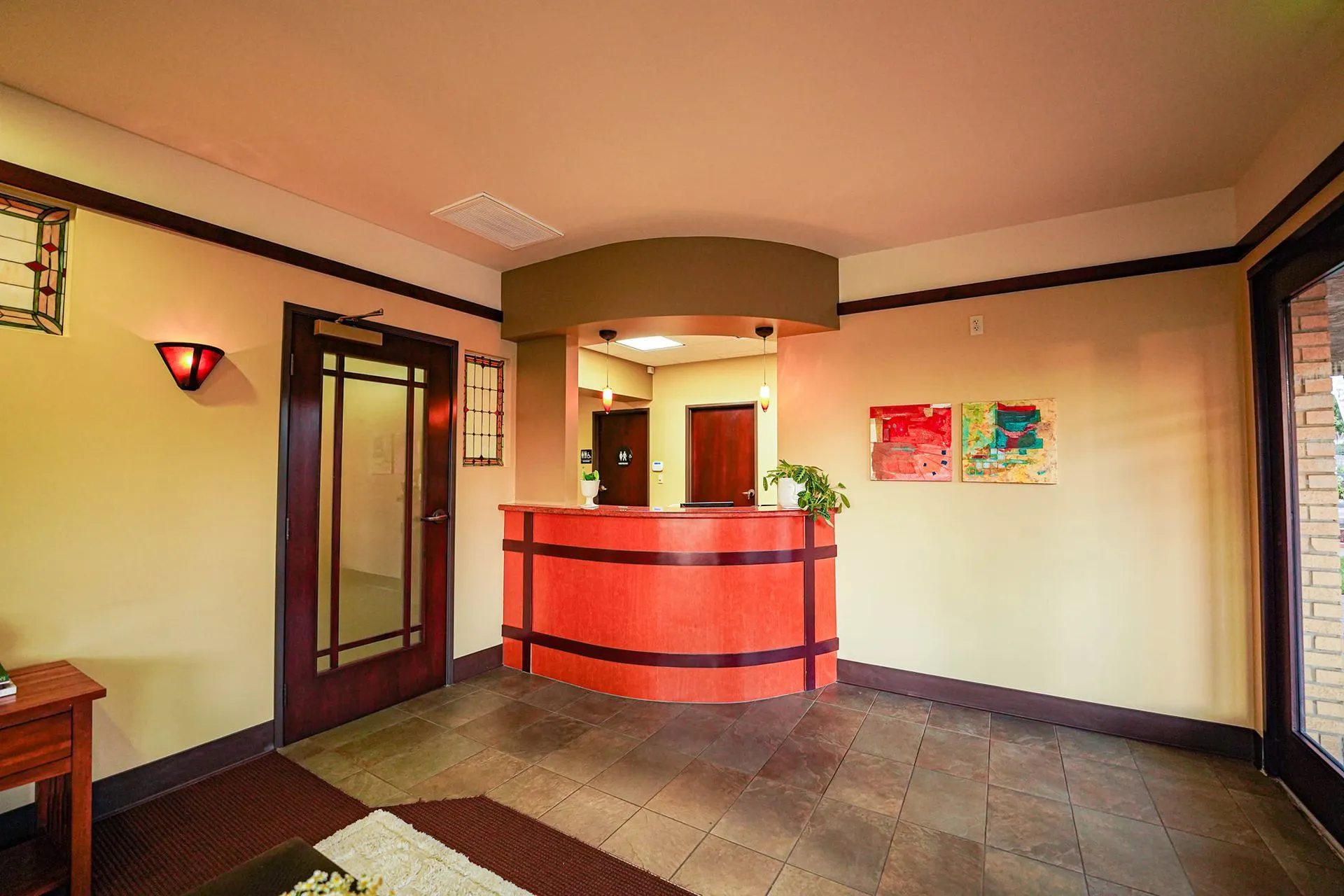 Warm lobby with a curved front desk, stained glass accents, and colorful artwork at Kind Dental of La Mesa in La Mesa, CA