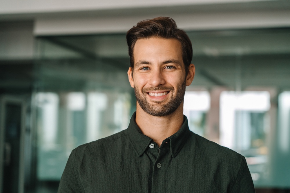 Dental Bonding in La Mesa, CA: Confident Everyday Smile Smiling bearded man in a dark green shirt at a modern office, reflecting the confidence of dental bonding in La Mesa, CA