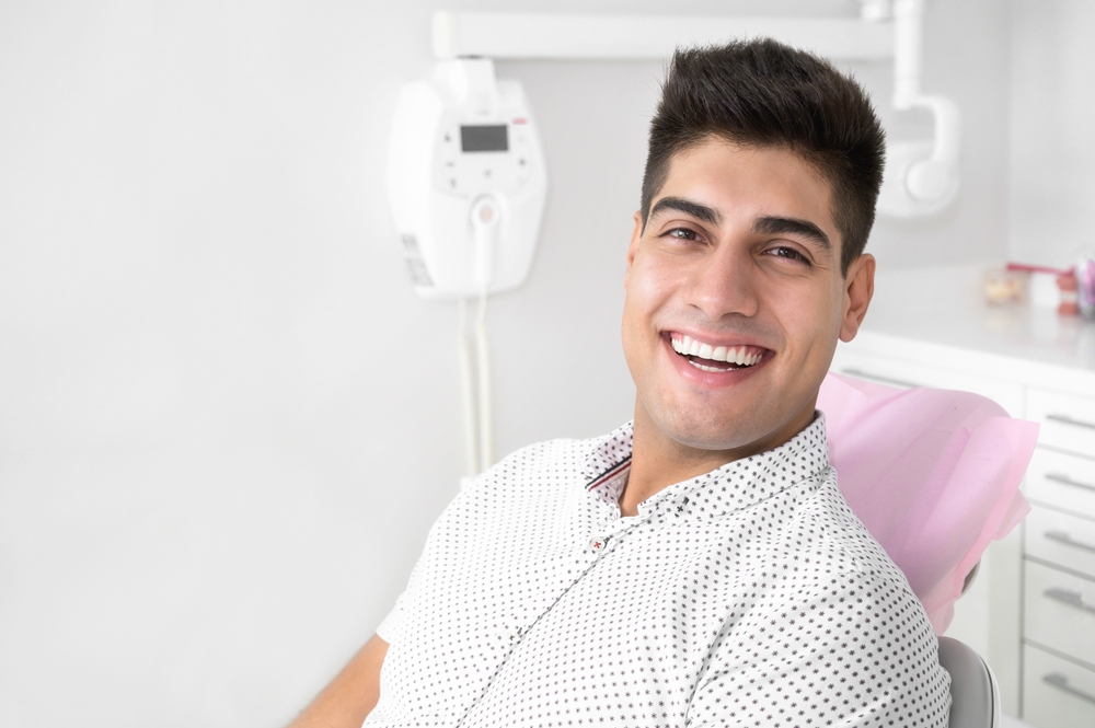 Smiling young man in a polka-dot shirt seated in a dental chair at an office offering inlays and onlays in La Mesa, CA