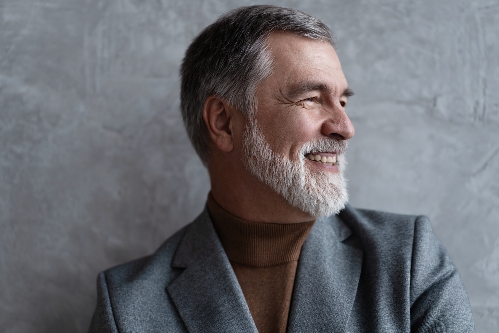 Smiling mature man with a gray beard and gray blazer, representing the confident smiles created by a dentist in La Mesa, CA