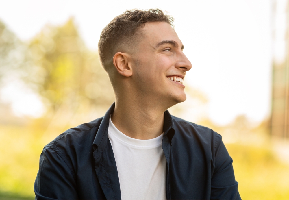 Confident Smile Outdoors, Cosmetic Dental Care in La Mesa, CA Young man in a navy shirt smiling in profile outdoors, reflecting the confidence cosmetic dental care in La Mesa, CA can bring